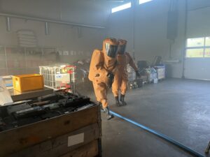 To røykdykkere kledd i oransje kjemikaliedrakter er inne på farlig avfall-mottaket på Årabrot. I forbindelse med øvelsen er luften fylt med røyk.